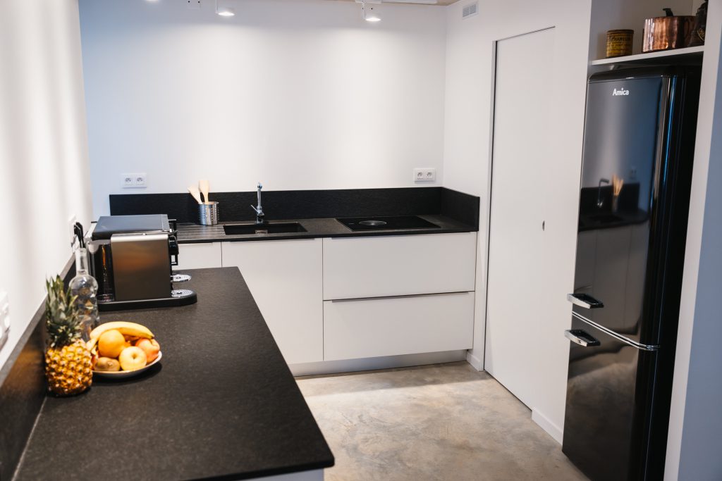 La cuisine moderne de la Maison des Cassiers, au sein de l’Hôtel Les Fleurines à Villefranche-de-Rouergue, Aveyron, offre un design épuré et des équipements de qualité. Son plan de travail en pierre, son réfrigérateur, ses plaques de cuisson et sa machine à café en font un espace idéal pour préparer des repas conviviaux.