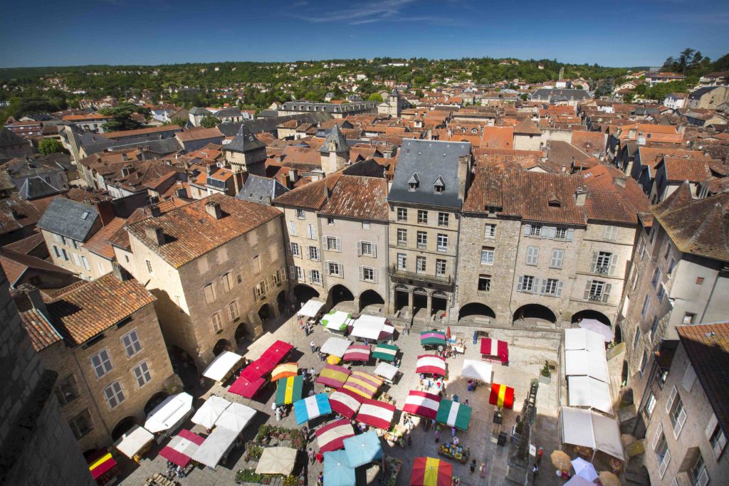 Vue sur la Place Notre-Dame à Villefranche-de-Rouergue, cœur vibrant de la ville en Aveyron, célèbre pour ses arcades majestueuses et son marché hebdomadaire, classé parmi les plus beaux marchés d’Occitanie. Un lieu animé et authentique qui incarne le charme de la bastide.
