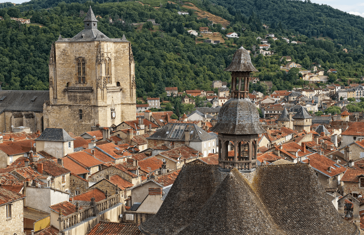 Vue depuis la promenade du Petit Languedoc, à quelques pas de l'Hôtel Les Fleurines, avec le clocher emblématique de la chapelle des Pénitents Noirs au premier plan et la majestueuse collégiale Notre-Dame en arrière-plan, symboles du patrimoine de Villefranche-de-Rouergue en Aveyron.