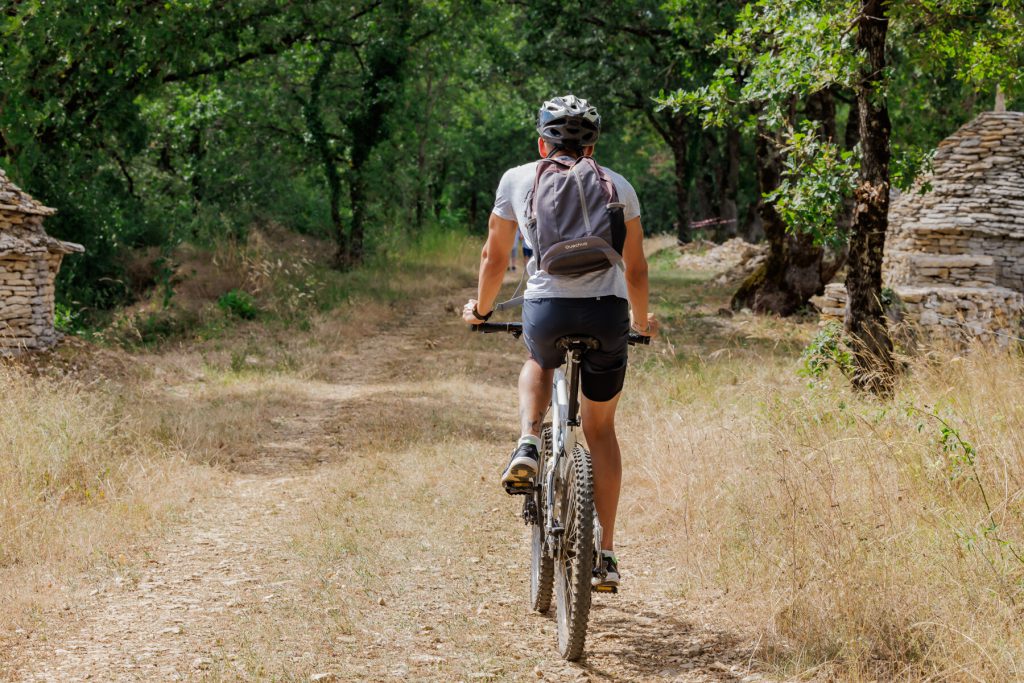 Balade à vélo sur le Causse près de Villefranche-de-Rouergue, un cycliste explore un sentier authentique, entre caselles en pierre sèche et chênes majestueux. Une escapade nature idéale pour un tourisme vert inoubliable, au cœur de l'Aveyron, près de l'Hôtel Les Fleurines.