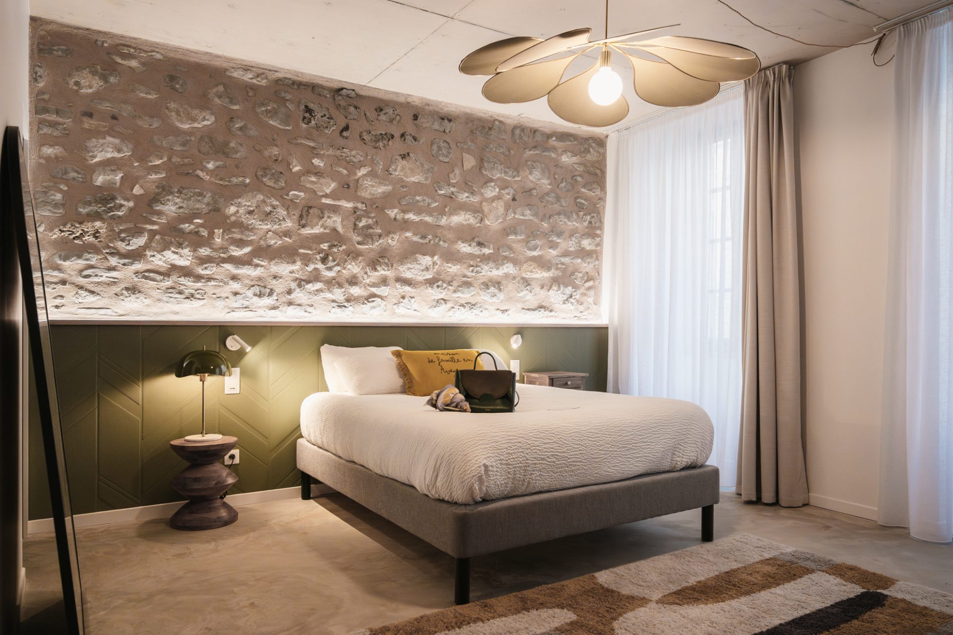 Chambre élégante et contemporaine de l’Hôtel Les Fleurines à Villefranche-de-Rouergue, dans l’Aveyron, avec mur en pierre apparente, éclairage doux et décoration raffinée aux teintes naturelles.